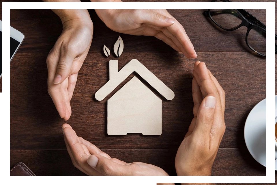 A group of hands surrounding a paper cut out house.