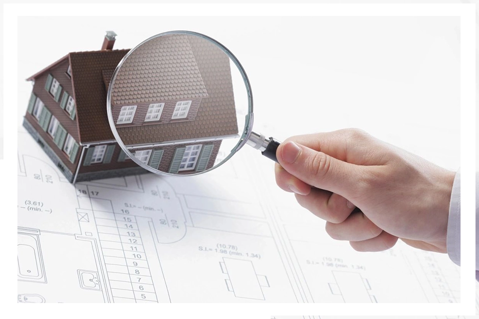 A person holding a magnifying glass over a house.