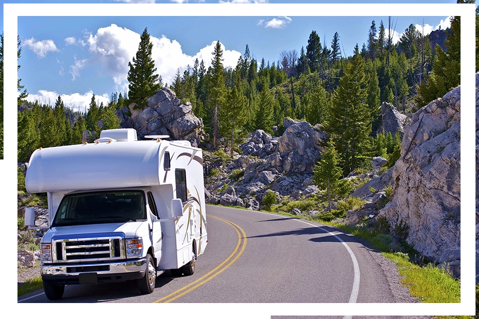 A white rv driving down the road near some trees.