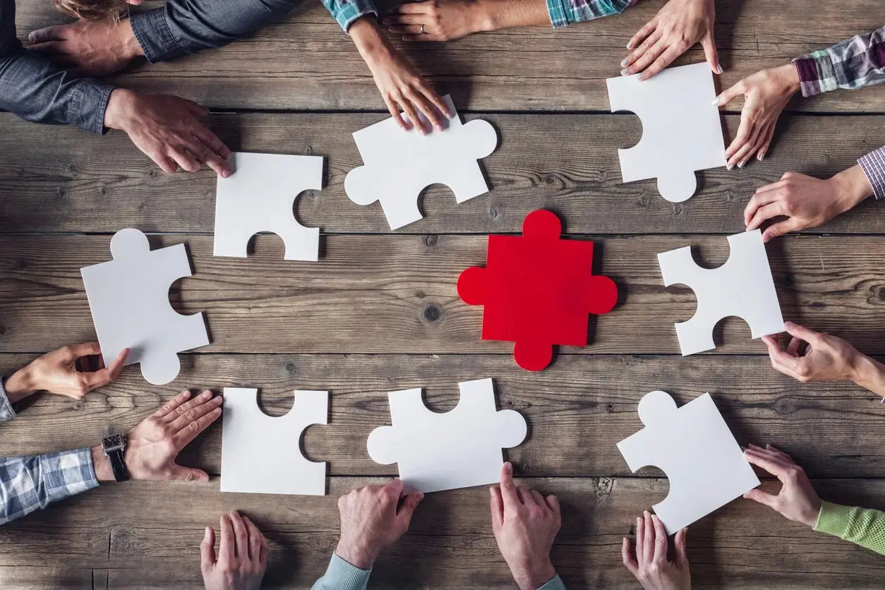 A group of people sitting around a table with puzzle pieces.